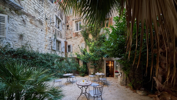 A courtyard with stone buildings, outdoor seating, and greenery. - Villa Split Heritage Hotel (Split)