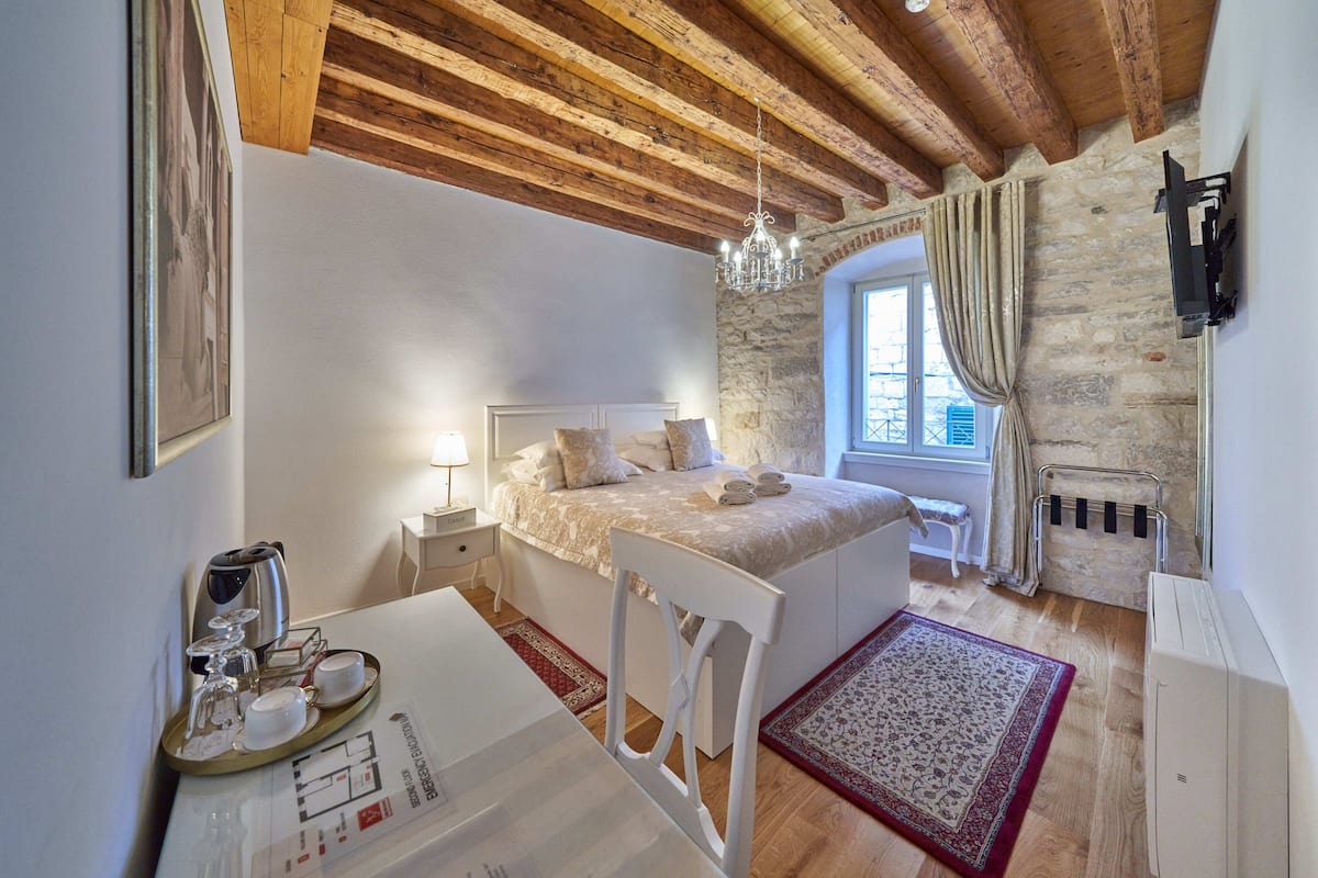 Une chambre confortable avec un plafond en bois, un mur en pierre, un lit avec des oreillers, une table de chevet avec une lampe et une fenêtre avec des rideaux.