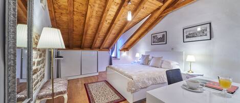 A bedroom with a wooden ceiling, a bed, bedside tables, a lamp, a mirror, and a framed picture on the wall.