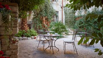 Un patio al aire libre con paredes de piedra, plantas en macetas y mesas y sillas de metal.