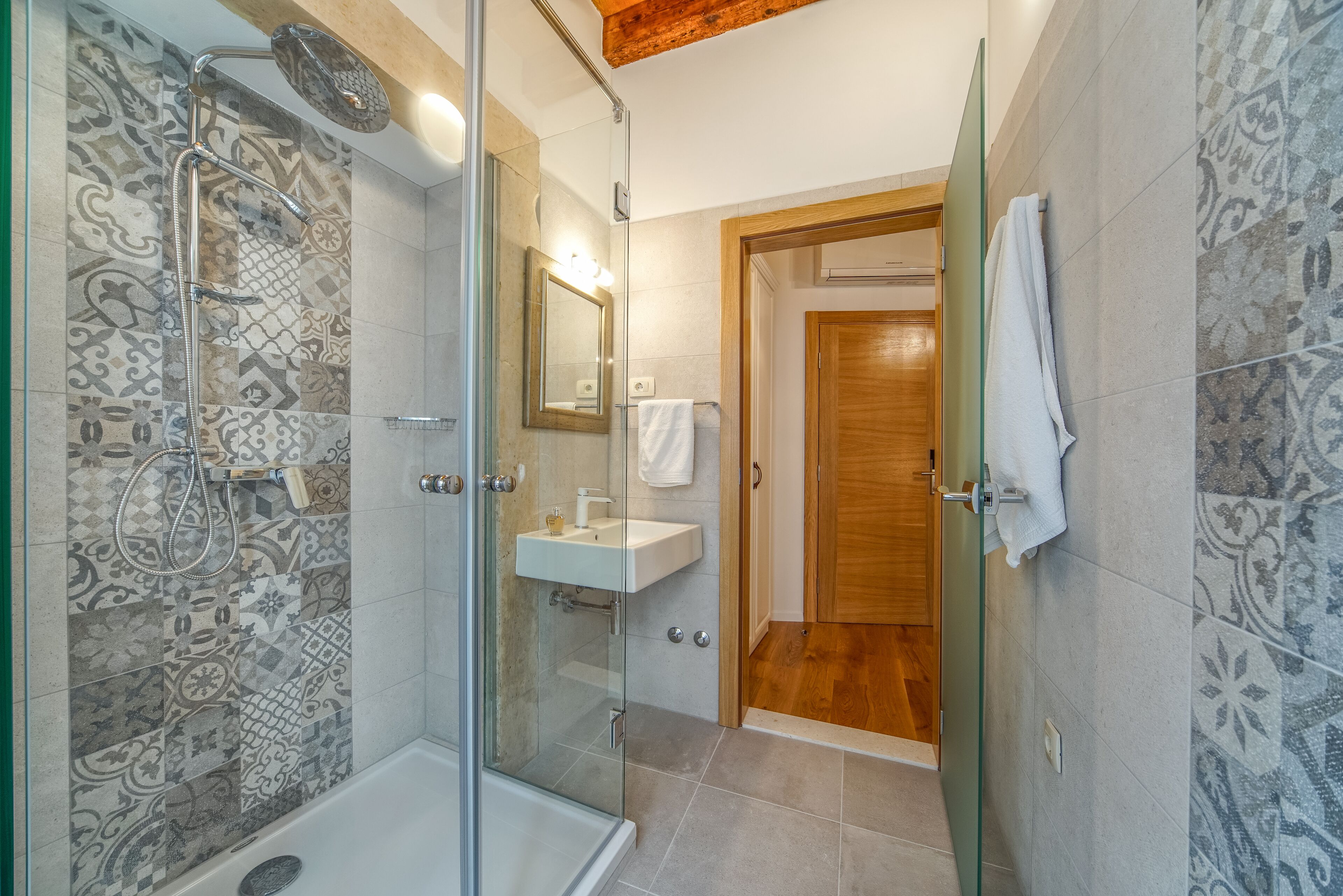Une salle de bain moderne avec une douche à parois de verre, une porte en bois et des carreaux décorés.