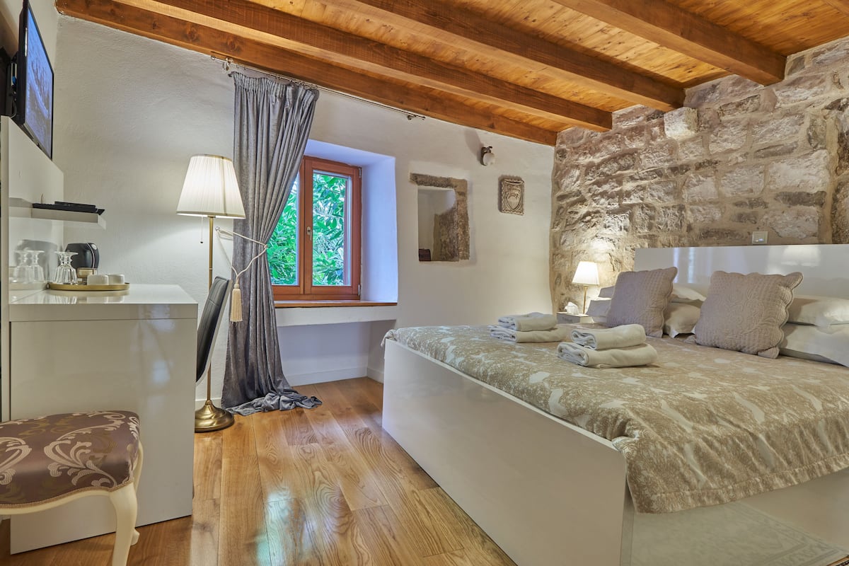 Une chambre à coucher avec un lit, une fenêtre, un mur en pierre, un bureau avec une lampe et une chaise.