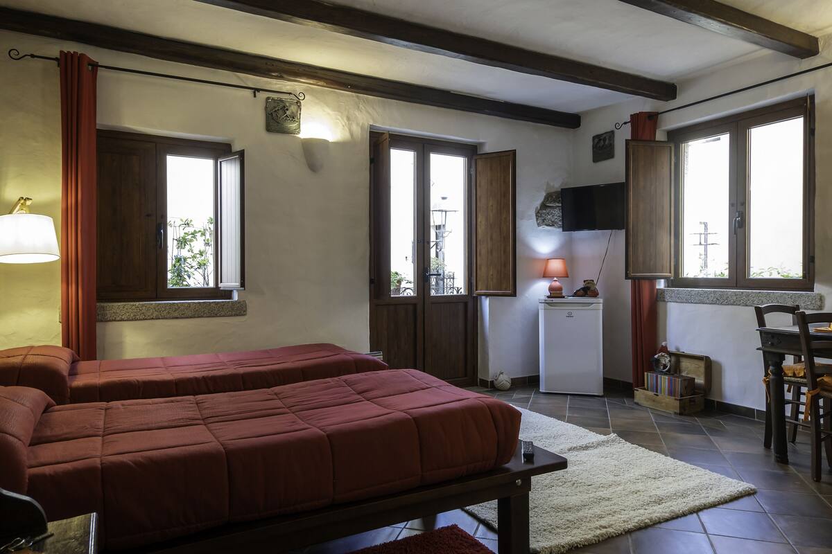A room with two beds, a small kitchenette, and a dining area.