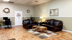 A room with two leather sofas, a wooden coffee table, a clock, a mirror, and a door with a welcome sign.