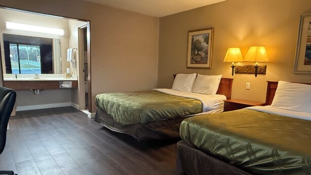 A hotel room with two beds, a desk, a chair, a mirror, and a painting on the wall.