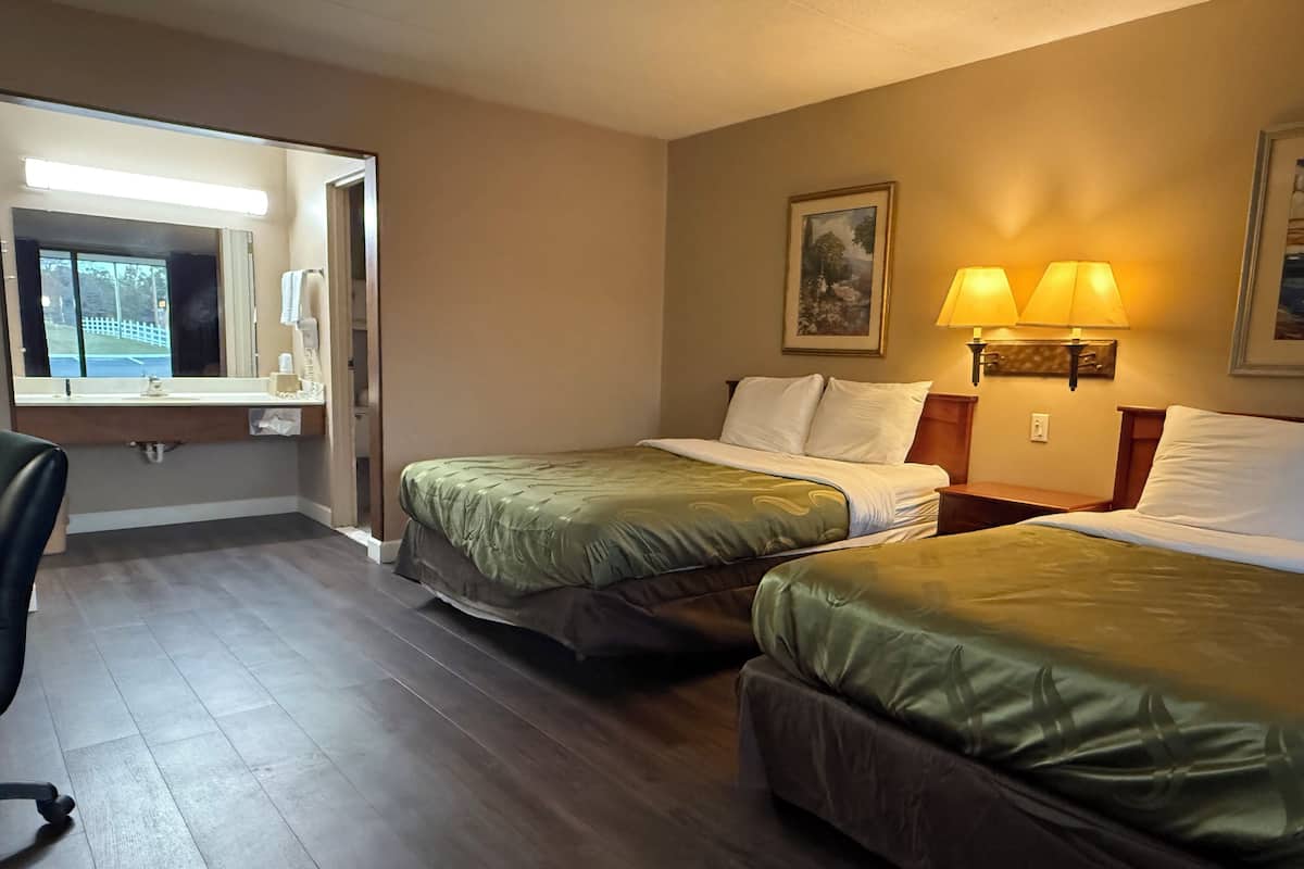 A hotel room with two beds, a desk, a chair, a mirror, and a painting on the wall.