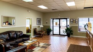 A lobby with a leather sofa, a coffee table, a lamp, and a door leading outside.