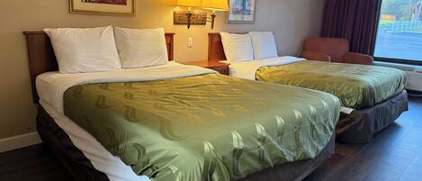 A hotel room with two beds, a large window with curtains, and two wall-mounted lamps.