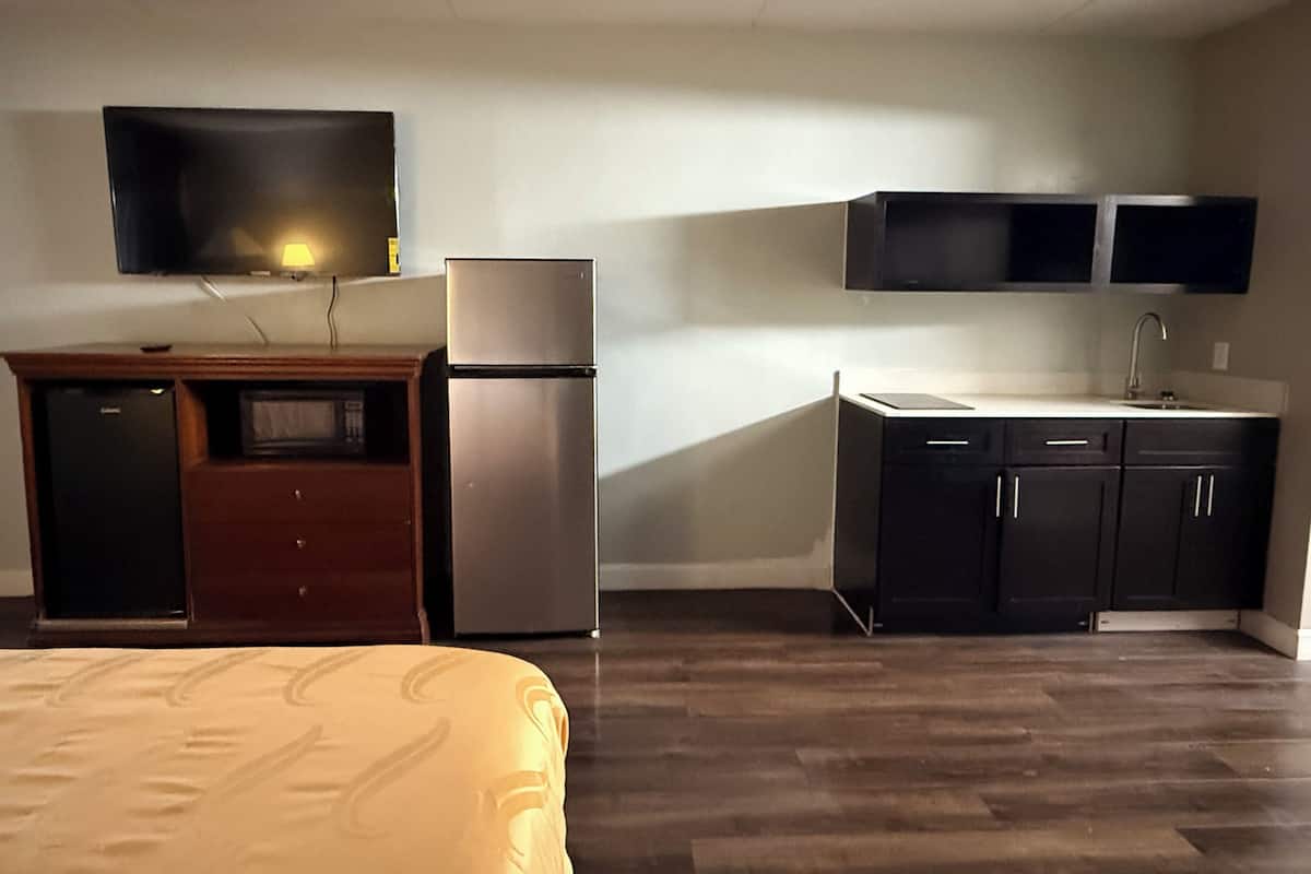 A compact hotel room with a bed, a kitchenette, a flat-screen TV, and a small refrigerator.