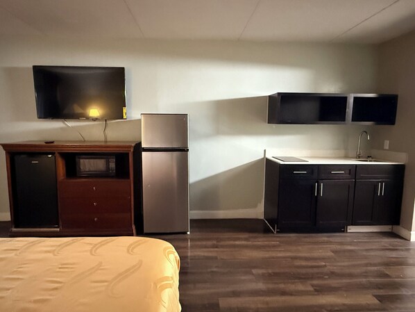 A compact hotel room with a bed, a kitchenette, a flat-screen TV, and a small refrigerator. - Paris Inn and Suites (Paris)