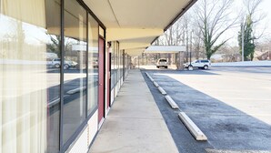 A covered walkway with large windows and a parking lot in the background.