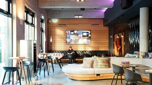 Un área de lounge moderna con un sofá curvo, sillas negras, un tablero de ajedrez y una pantalla grande mostrando contenido.