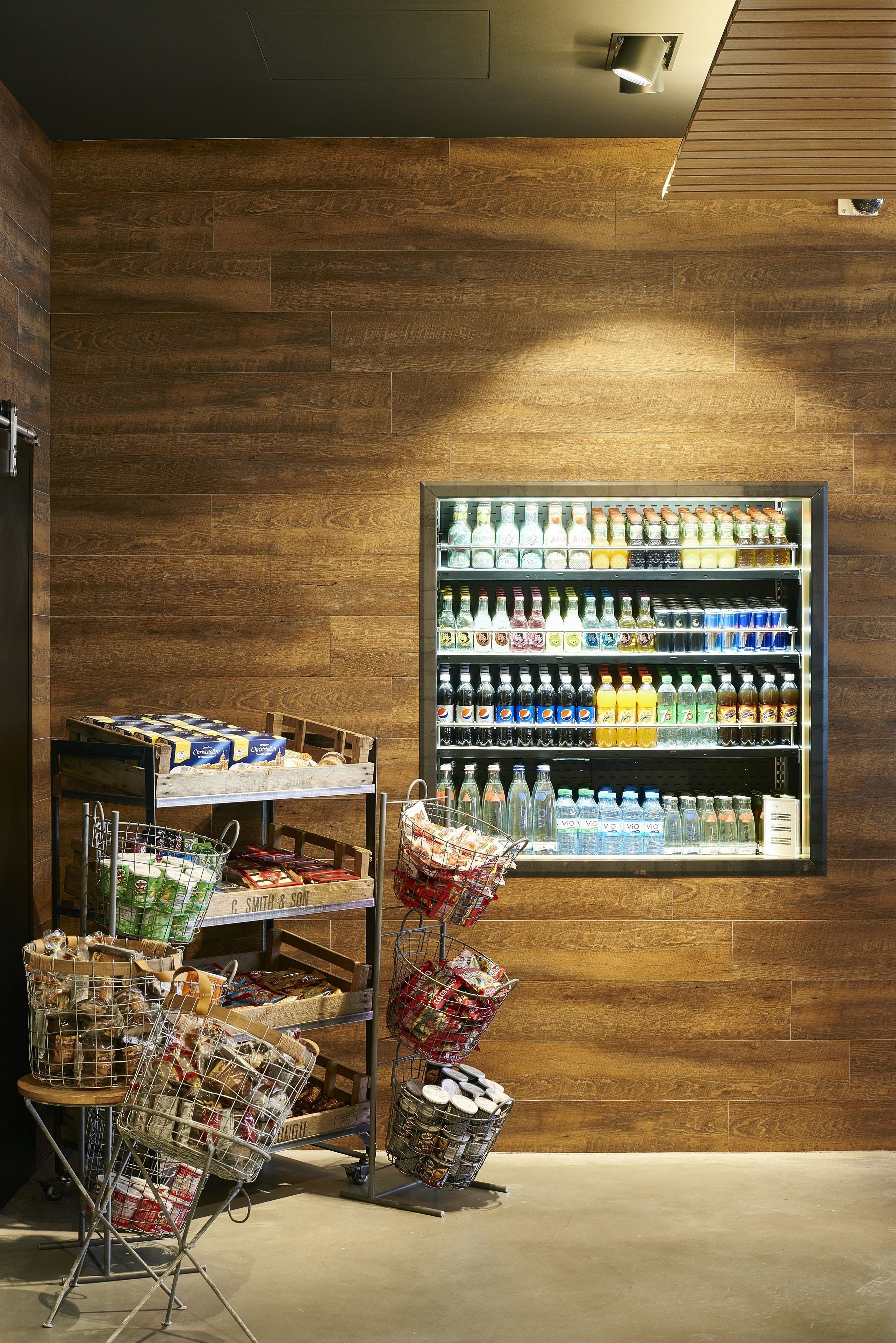 A grocery store interior with wooden flooring, a refrigerated beverage display, and various packaged goods on shelves.