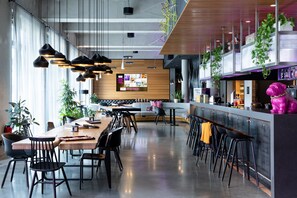 Un restaurante moderno con una larga mesa compartida, sillas negras, lámparas colgantes y una zona de bar con taburetes.