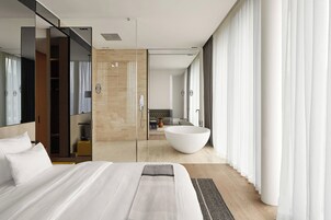 Quarto de hotel moderno com uma cama grande, um closet espaçoso, uma banheira grande e vista para o banheiro e a sala de estar.