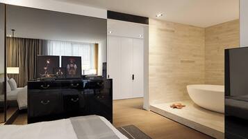 Une chambre d’hôtel moderne avec un grand lit, une commode noire, un grand miroir, une armoire blanche, un mur d’accent en bois et une grande baignoire.
