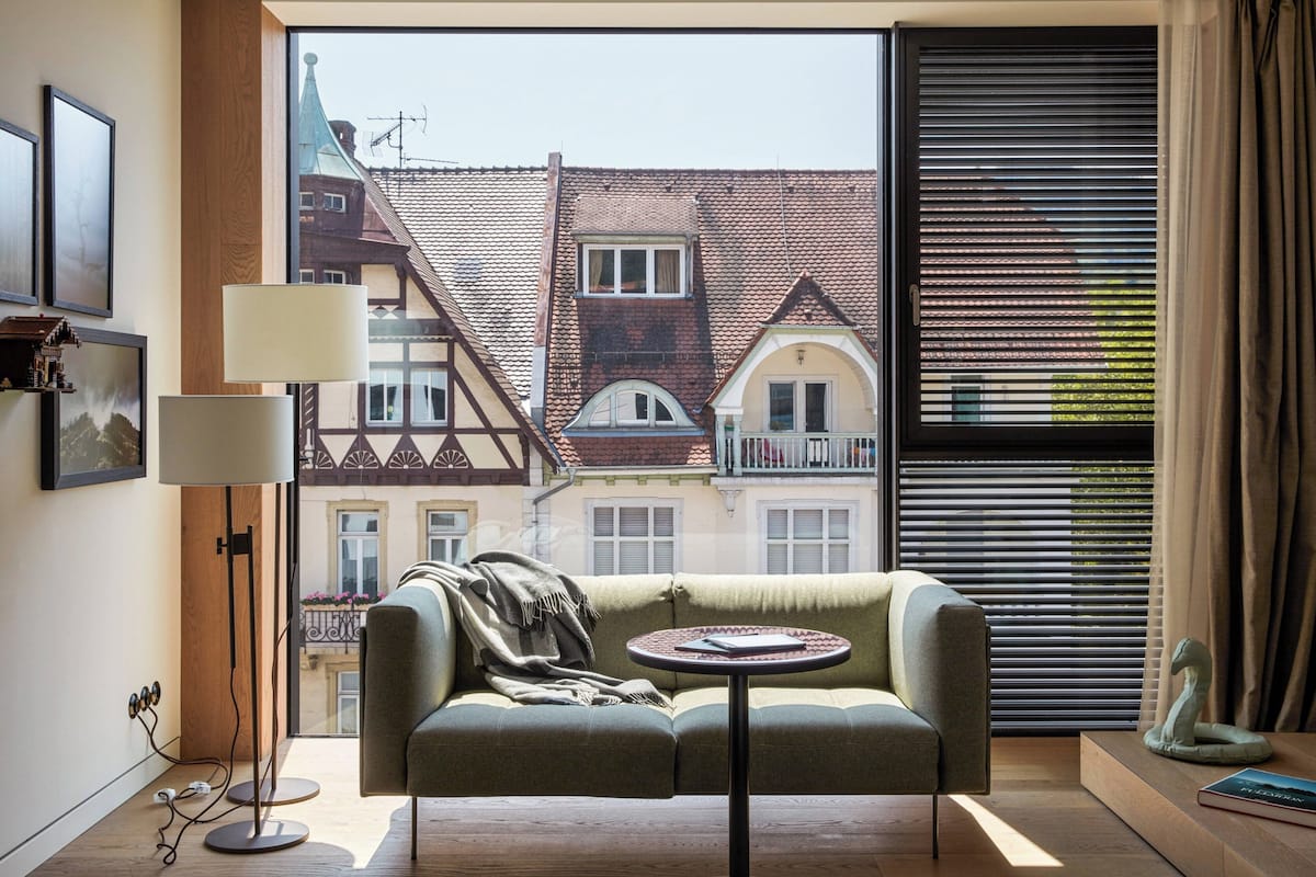 Une pièce chaleureuse avec un canapé et une petite table, un lampadaire et une vue sur des bâtiments traditionnels par la fenêtre.