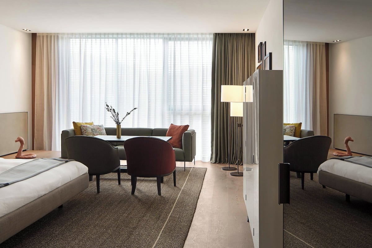 Une chambre d’hôtel avec deux lits, un canapé, une table à manger et une grande fenêtre avec des rideaux.