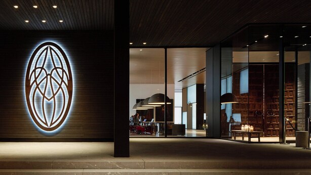 A modern interior with a prominent logo on the wall, a seating area with tables, and a staircase leading to an upper level. - Roomers Baden-Baden, Autograph Collection (Baden-Baden)