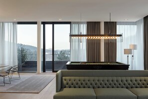 Un salon moderne avec un canapé vert, une table de billard et une vue sur le paysage urbain, visible à travers de grandes fenêtres.