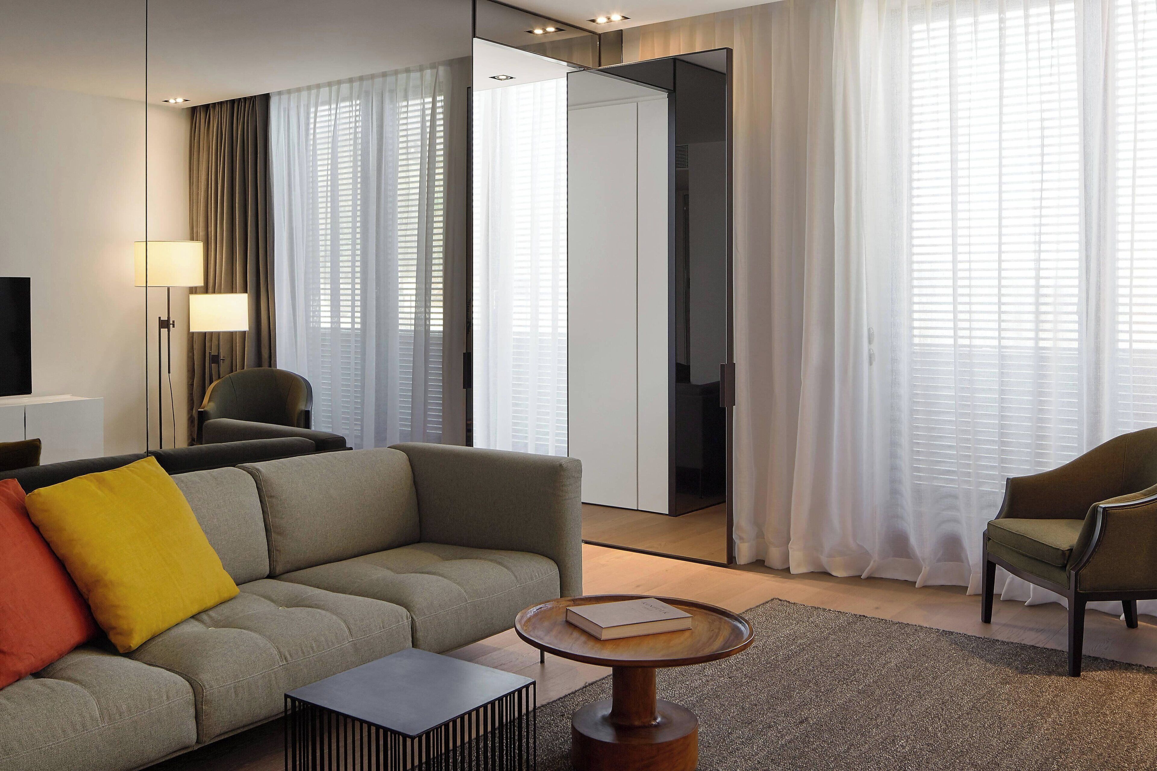 A modern hotel room with a sofa, armchairs, a coffee table, and a TV.