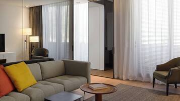 A modern hotel room with a sofa, armchairs, a coffee table, and a TV.