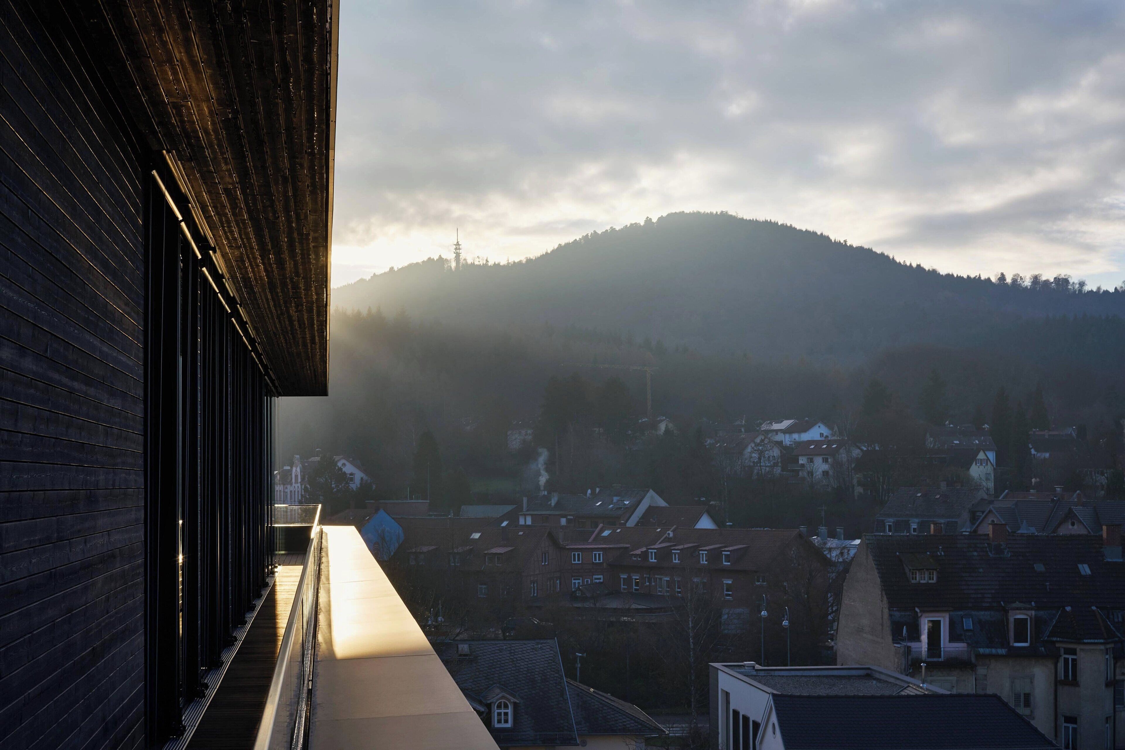 Een gebouw met een lang, smal balkon met uitzicht op een stad en een heuvel.