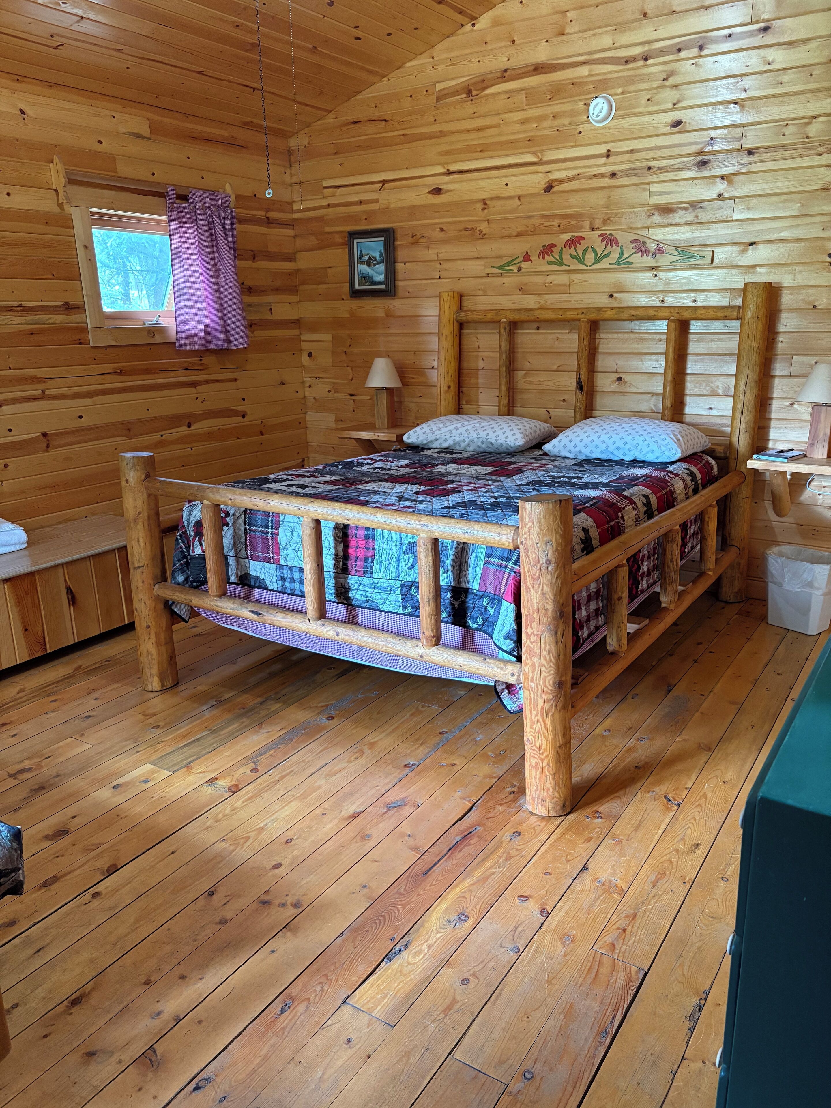 Ein Zimmer in einer Holzhütte mit einem Bett, Holzvertäfelung, einem Fenster und einer Lampe.
