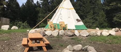 Una tenda indiana con un tavolo da picnic e due sedie di fronte, circondata da rocce e alberi.