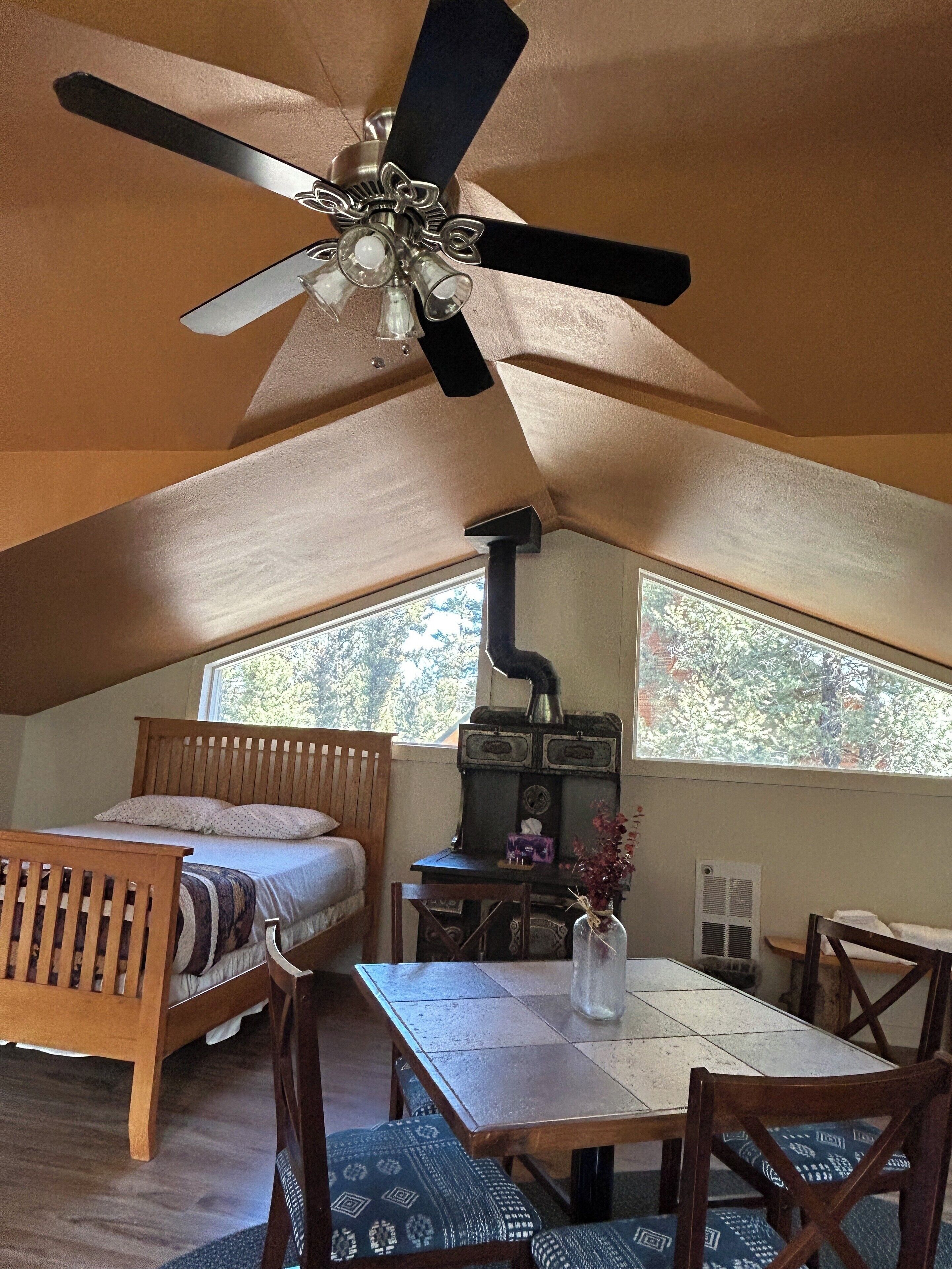 A cozy attic bedroom with a bed, wooden furniture, a table, and a ceiling fan.