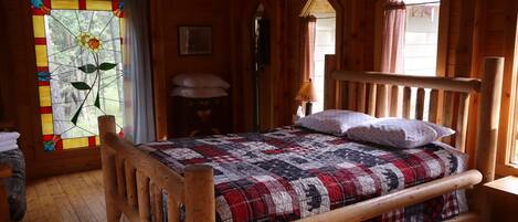 Un dormitorio de cabaña de madera con una cama, un ventanal de vitral y un cabecero de madera.