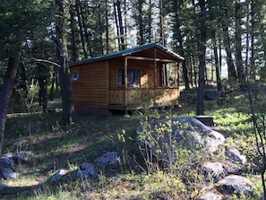Eine Holzhütte mit Veranda, umgeben von Bäumen und Felsen in einer Waldlandschaft.