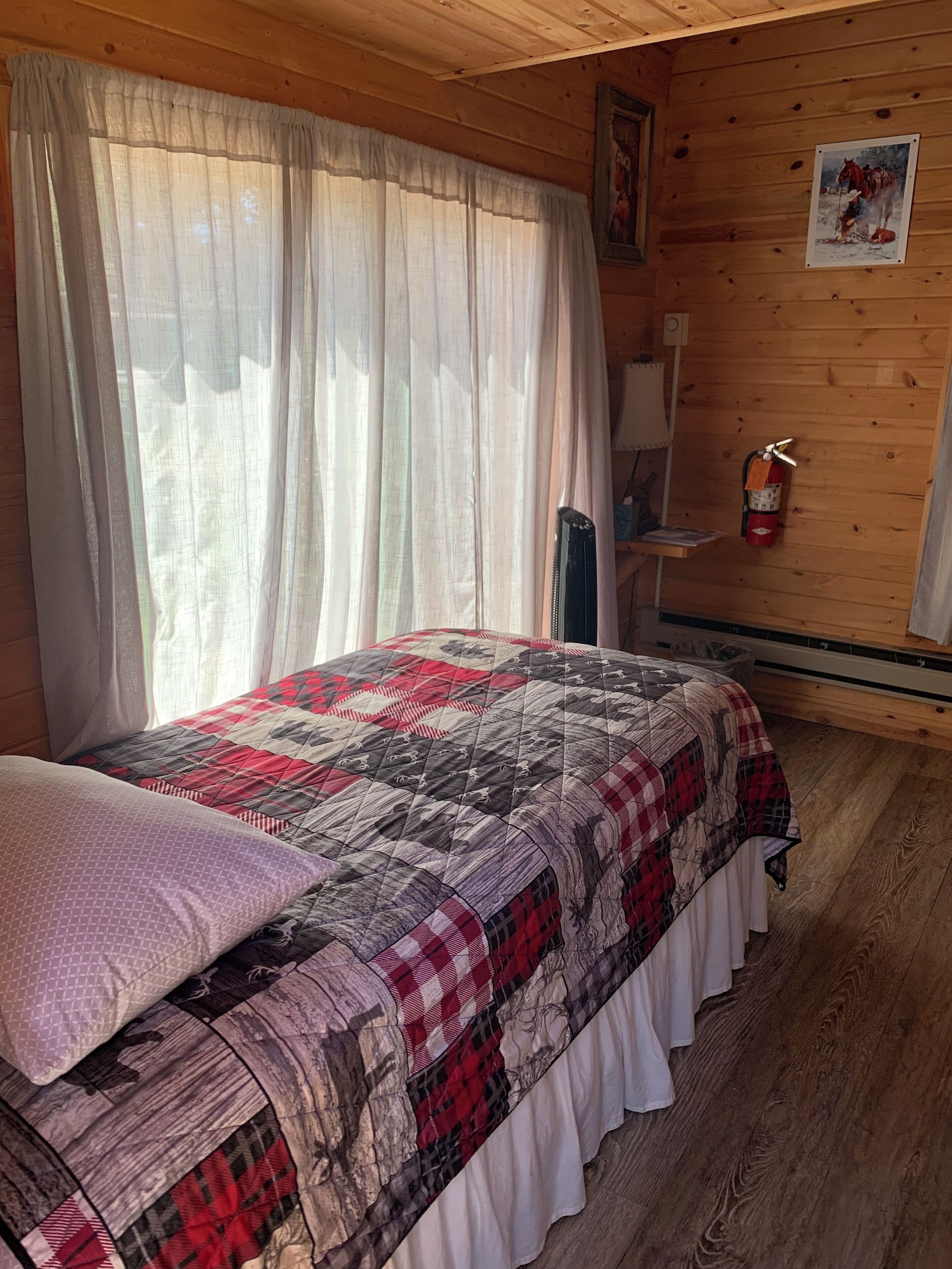 A cozy room with a bed, a fire extinguisher, and a painting on the wall.