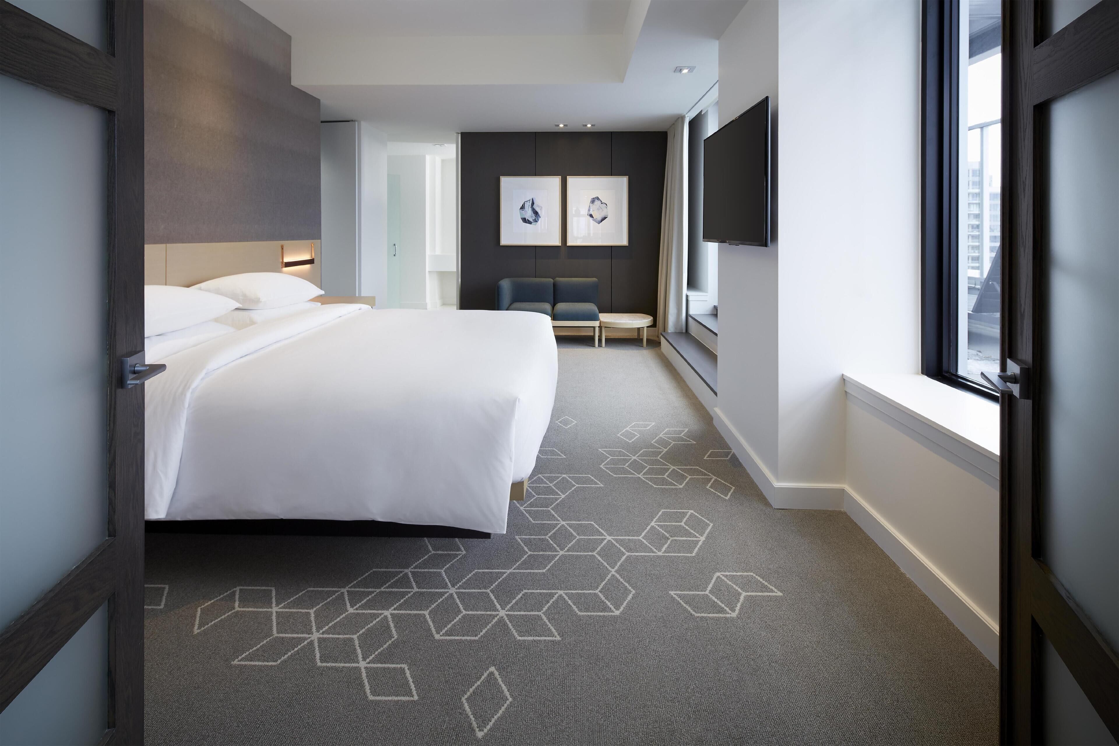 Quarto de hotel moderno com uma cama grande, área de estar e TV.