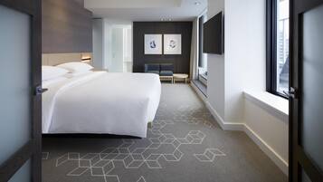 Quarto de hotel moderno com uma cama grande, área de estar e TV.