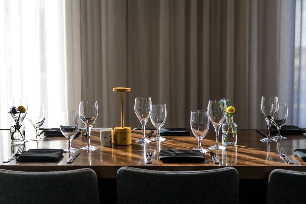 A dining table set with wine glasses, a candle, and a vase with flowers.