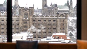 Vista de un paisaje urbano a través de una ventana, con edificios históricos y una imponente torre del reloj.