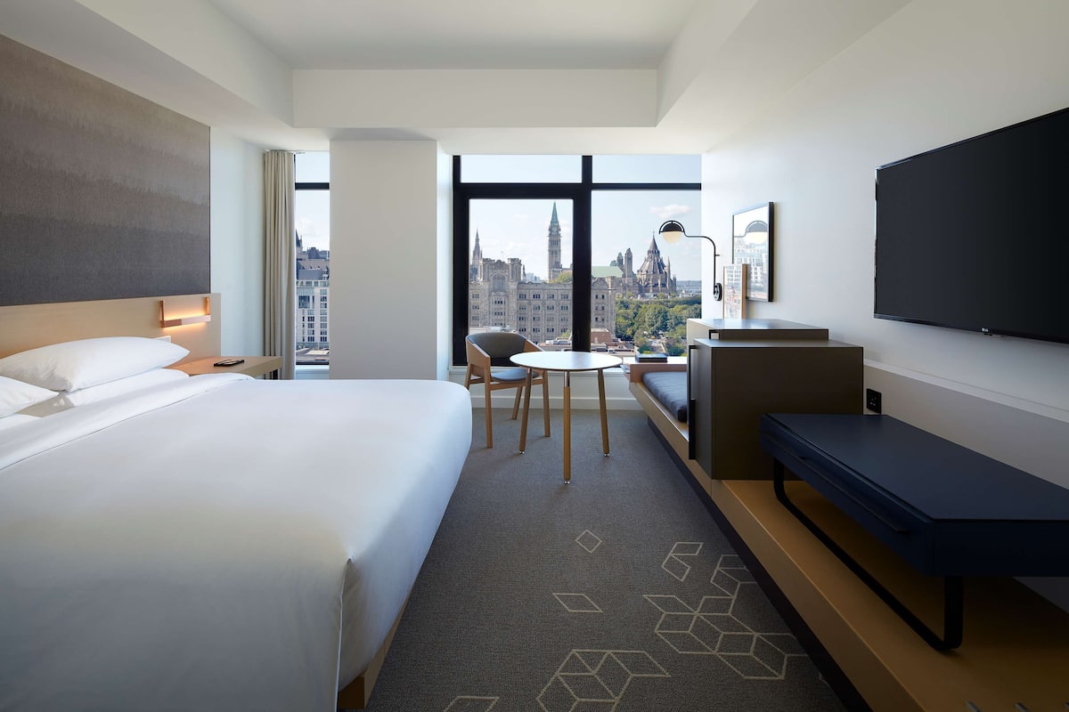 A hotel room with a large bed, a desk, a chair, a sofa, and a TV.