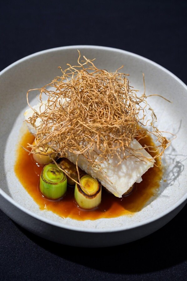 Un plato con pescado, cebollines y salsa.