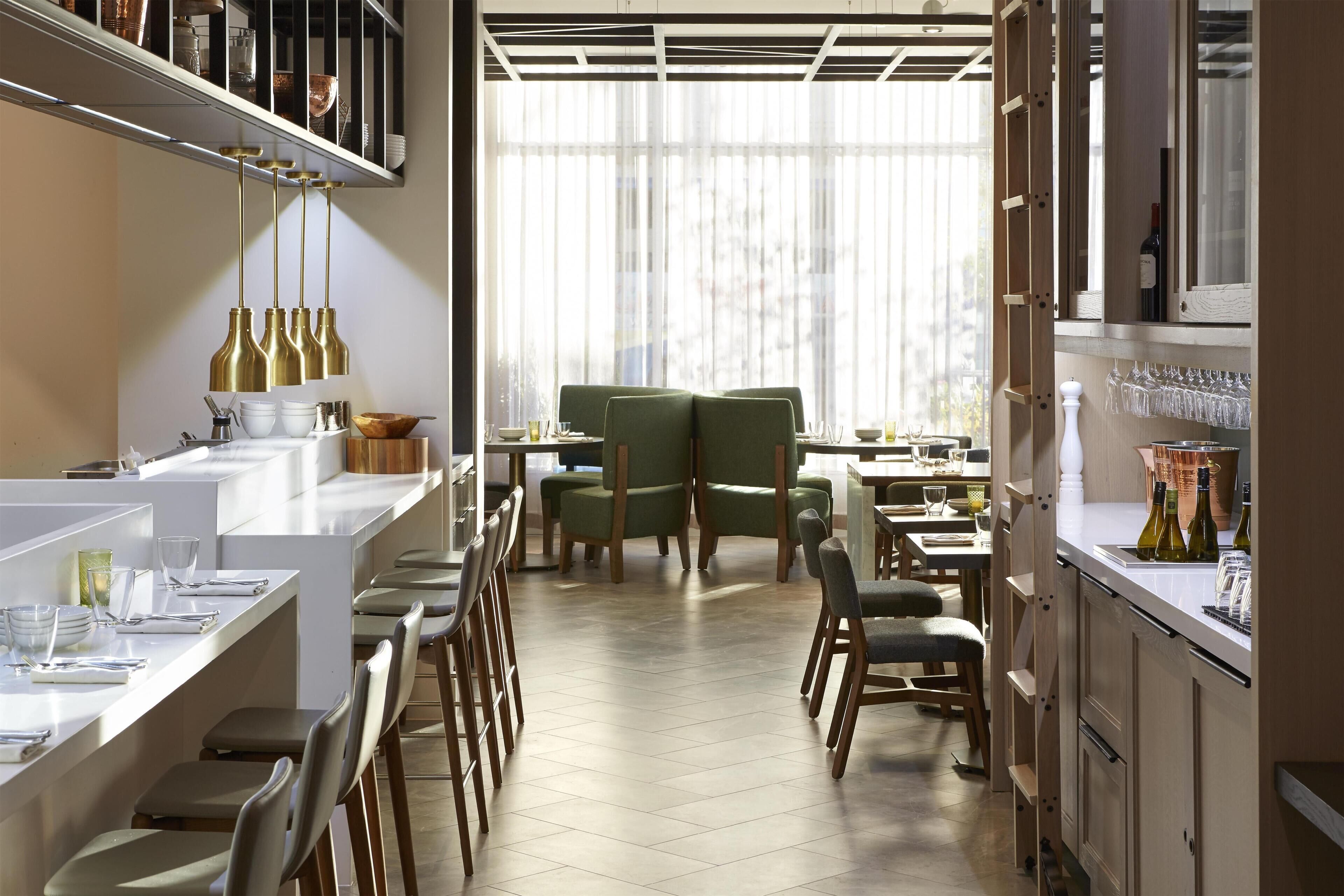 A modern restaurant with a central dining area, multiple seating options, and a bar area with wine bottles.
