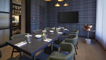 Una sala de conferencias con una mesa larga, sillas, una pantalla de televisión y un cuenco de cobre con botellas sobre un soporte.