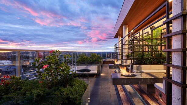 Terraza en la azotea con mobiliario exterior, una chimenea y vistas a la ciudad al atardecer.