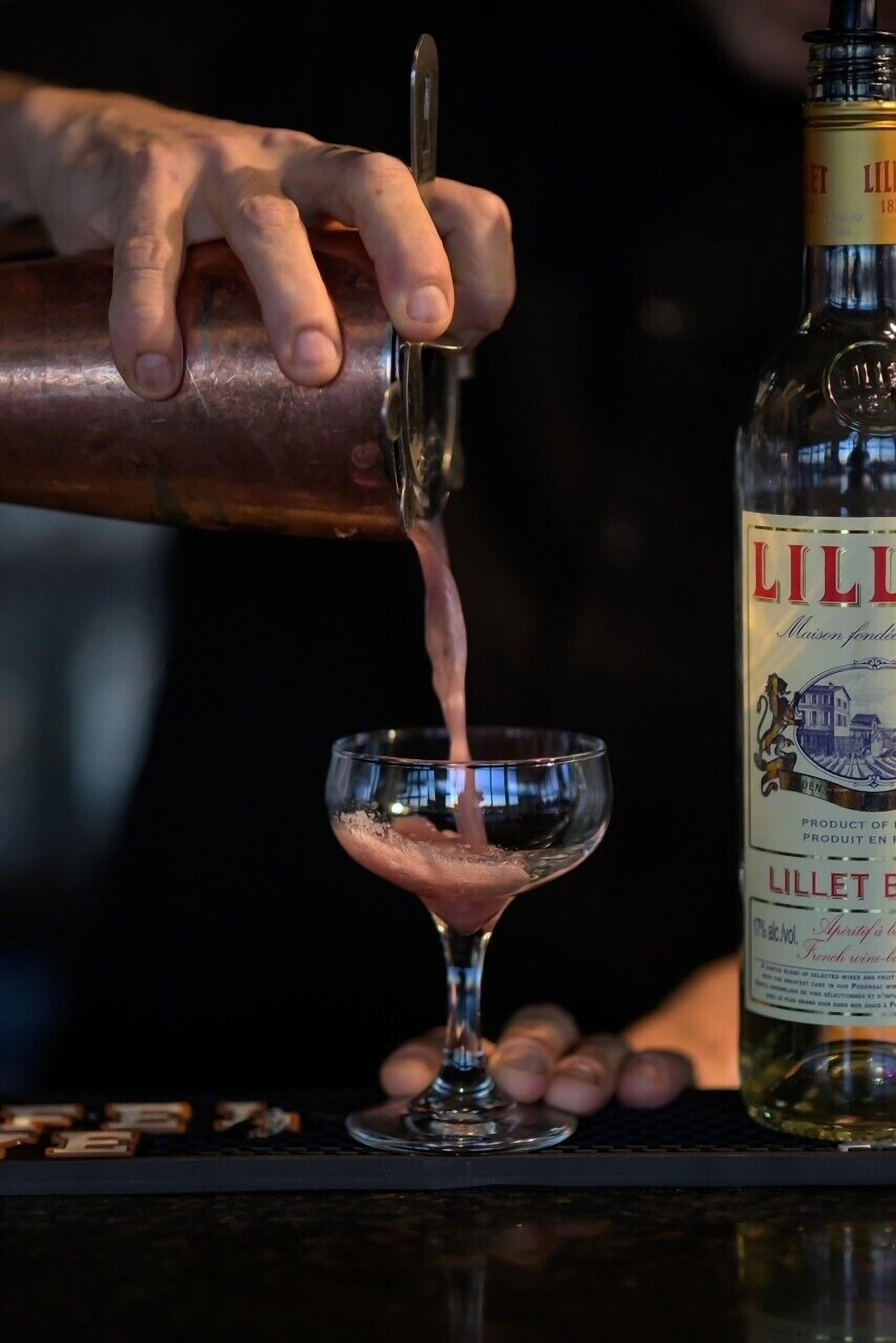 A hand pouring a drink from a bottle into a glass.