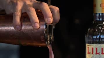 A hand pouring a drink from a bottle into a glass.
