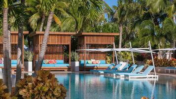 Uma área de piscina com espreguiçadeiras, cabanas de madeira e palmeiras.