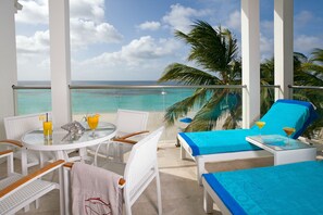 Un balcon avec vue sur l’océan, des meubles en osier blancs et une table avec des boissons.