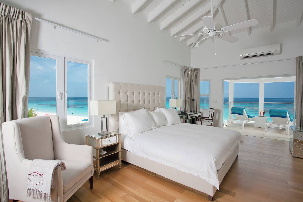 Un dormitorio espacioso con una cama grande, una zona de estar con vistas a la playa y un ventilador de techo.
