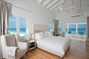 A spacious bedroom with a large bed, a sitting area with a view of the beach, and a ceiling fan.