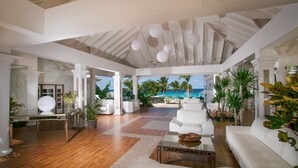 Un espacio habitable amplio con vista al océano, muebles blancos y plantas tropicales.