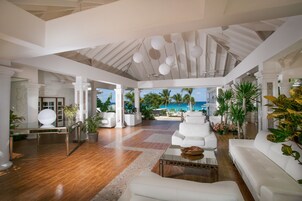 A spacious living area with a view of the ocean, white furniture, and tropical plants.